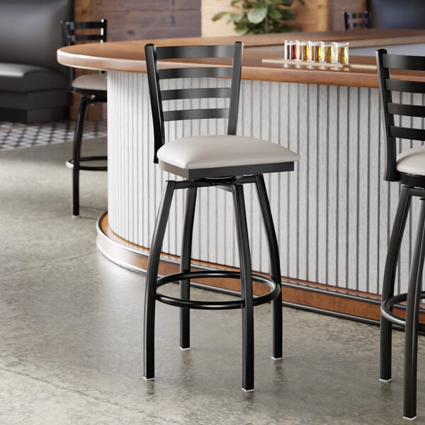 A black metal ladder back swivel bar stool with a light gray vinyl padded seat.