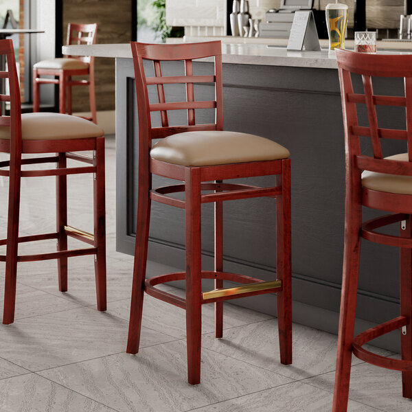 Three Lancaster Table & Seating mahogany wood bar stools with taupe vinyl seats at a counter.
