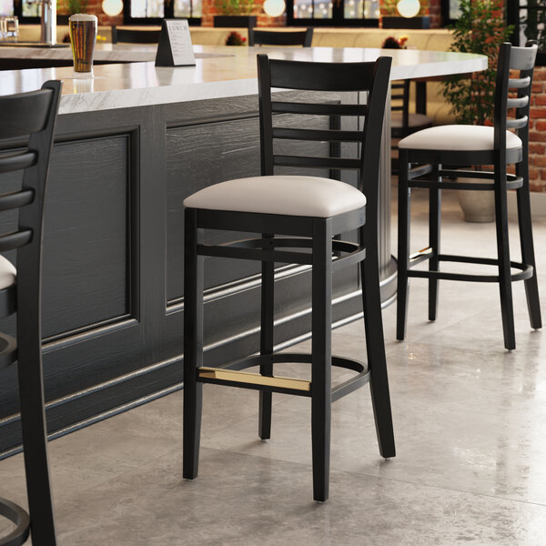 A Lancaster Table & Seating black wood ladder back bar stool with a light gray seat.