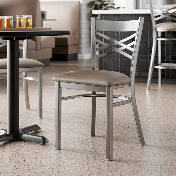 A metal cross back chair with a taupe vinyl padded seat and a clear coat finish.