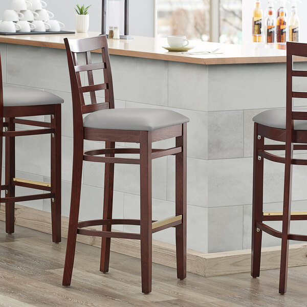 Three Lancaster Table & Seating mahogany wood window back bar stools with light gray vinyl seats.