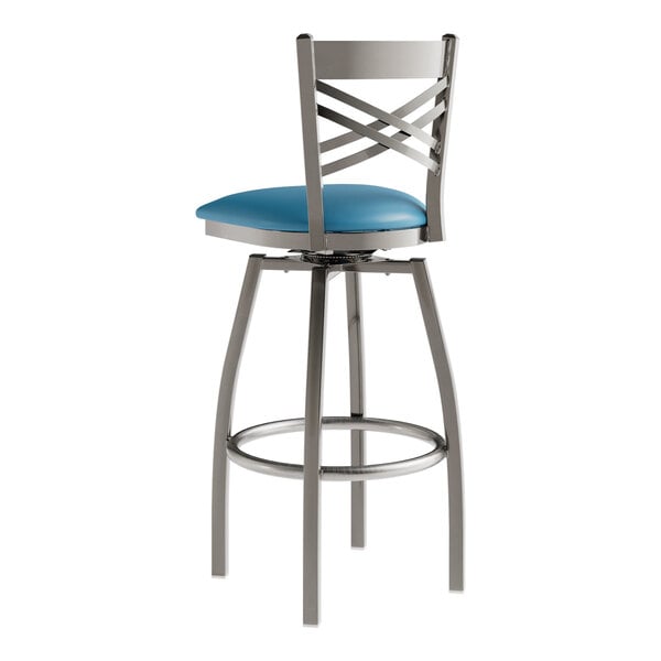 A Lancaster Table & Seating clear coat finish cross back swivel bar stool with a blue vinyl padded seat and chrome legs.
