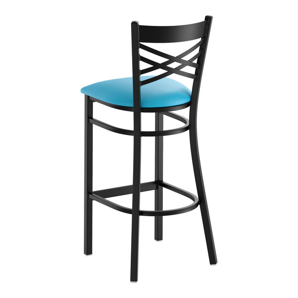 A black metal bar stool with a cross back design and a blue vinyl padded seat.