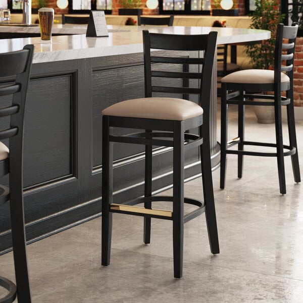 A Lancaster Table & Seating black wood bar stool with a tan vinyl seat.