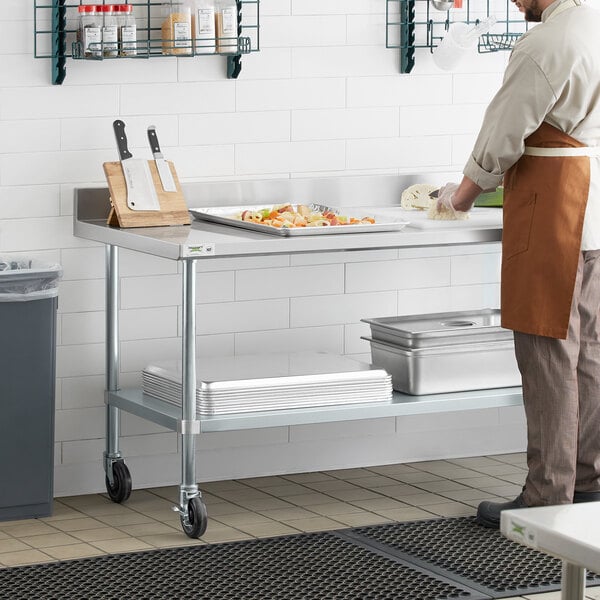 A man in a kitchen using a Regency stainless steel work table.