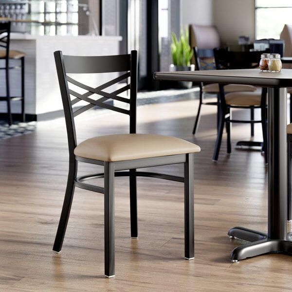 A black metal cross back chair with a taupe vinyl padded seat.