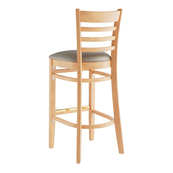 A Lancaster Table & Seating wooden bar stool with a dark gray cushion on the seat.