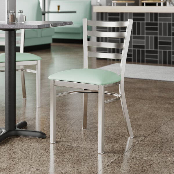 A Lancaster Table & Seating ladder back chair with a seafoam vinyl padded seat on a table in a restaurant.