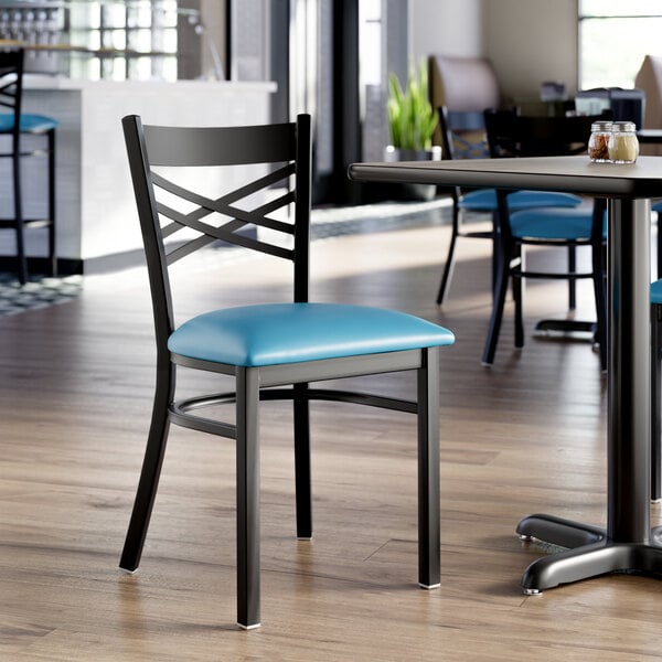 A black metal chair with a cross back design and a blue vinyl padded seat.