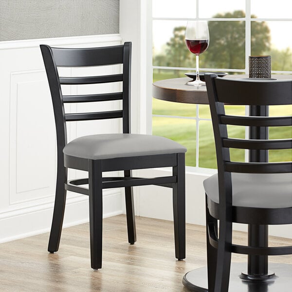 A close-up of a Lancaster Table & Seating black wood chair with a light gray cushion.