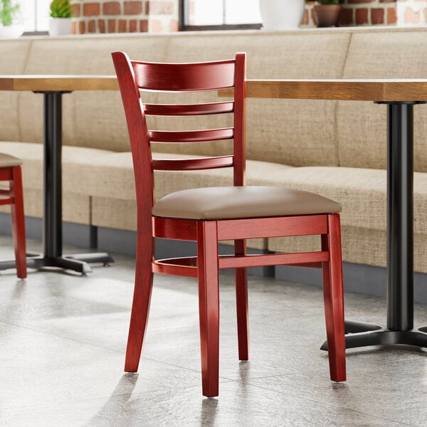 A Lancaster Table & Seating mahogany wood chair with a taupe vinyl seat on a table in a restaurant.