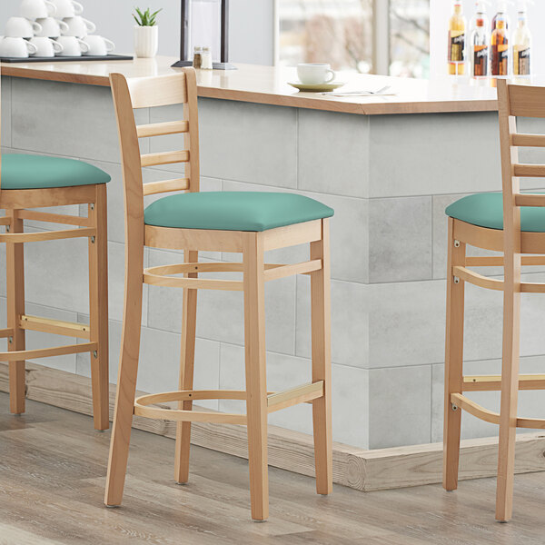 Three Lancaster Table & Seating wood ladder back bar stools with seafoam vinyl seats at a counter.