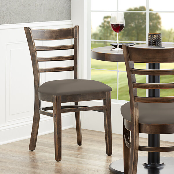 A pair of Lancaster Table & Seating vintage wood ladder back chairs with taupe vinyl seats at a table in a restaurant.