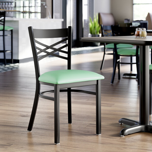 A black metal cross back chair with a 2 1/2 inch seafoam green vinyl padded seat.