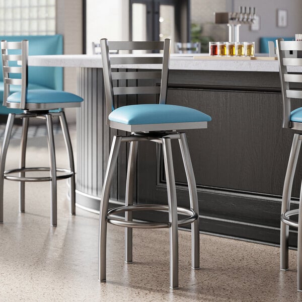 A group of three Lancaster Table & Seating blue vinyl padded bar stools with clear coat finish on the ladder backs.