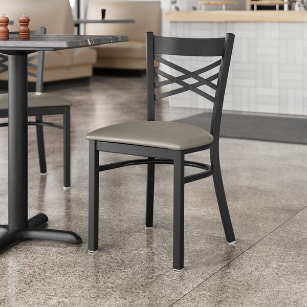 A Lancaster Table & Seating black cross back chair with dark gray vinyl padded seat at a table in a restaurant.