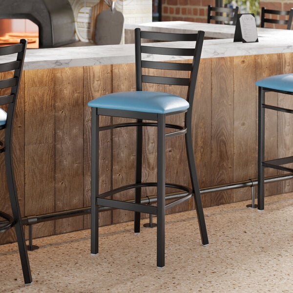 A black ladder back bar stool with a blue vinyl padded seat positioned at a counter.