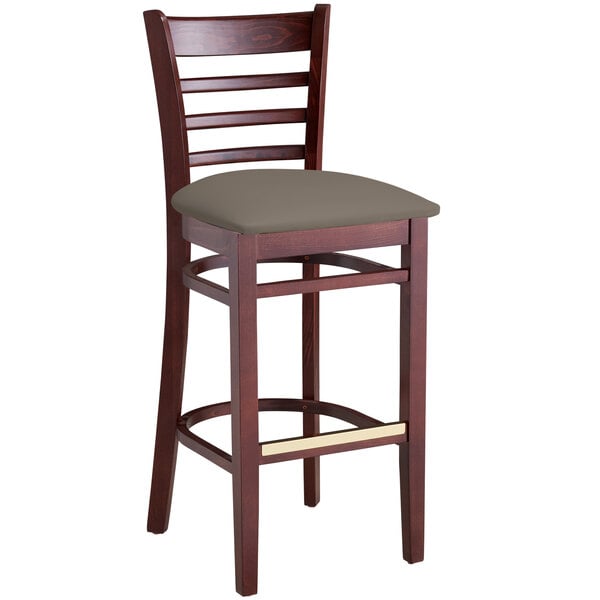A wooden bar stool with a taupe padded seat, featuring a mahogany finish and ladder back design, placed on a table in a bar.