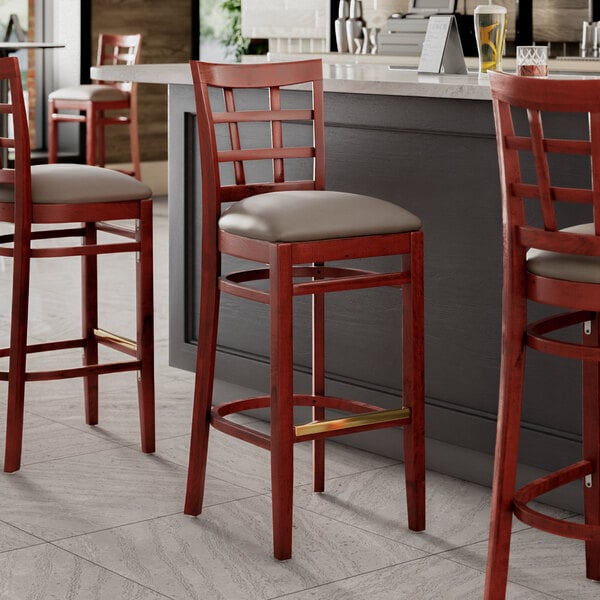 A group of three Lancaster Table & Seating mahogany wood bar stools with dark gray vinyl seats.
