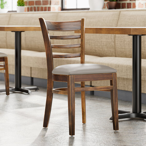 A Lancaster Table & Seating wooden chair with a dark gray vinyl seat at a table in a restaurant.