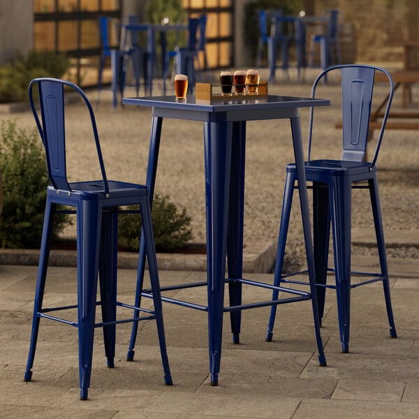 A blue metal Lancaster Table & Seating bar table and two chairs on a stone patio.