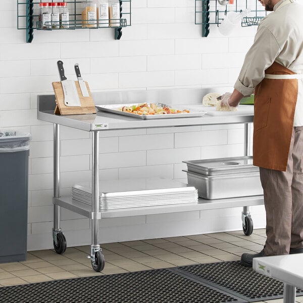 A man in an apron using a Regency stainless steel work table in a kitchen.