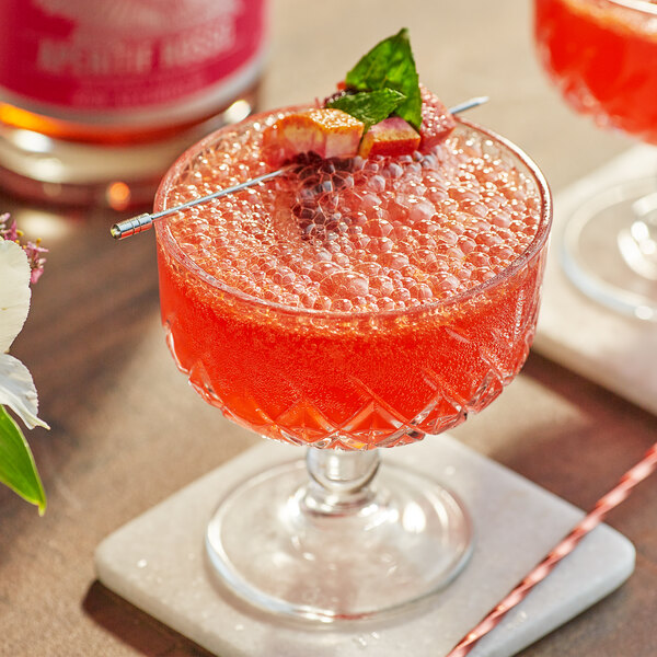 A glass of red Lyre's Aperitif with a strawberry on the rim and a red and white straw.