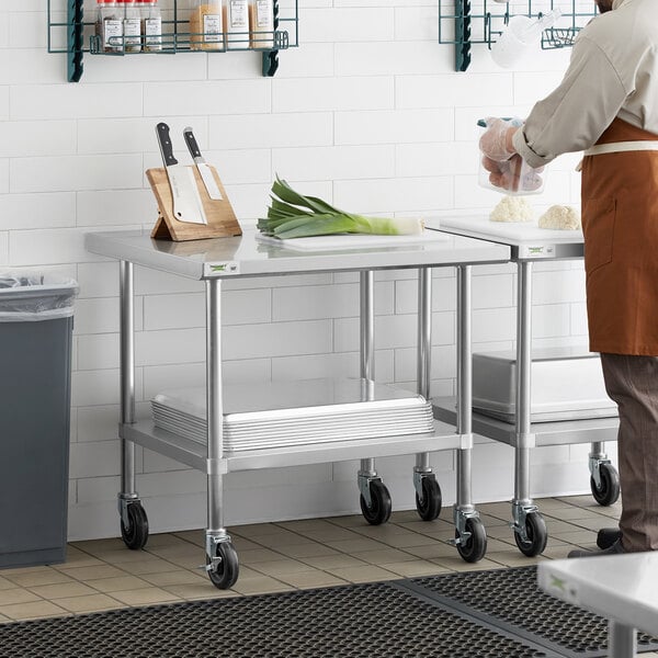 A man in an apron standing next to a Regency stainless steel work table with casters.