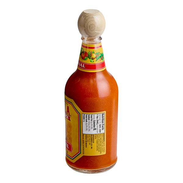 A glass bottle filled with orange hot sauce, featuring a wooden cap and colorful label with nutritional information visible.