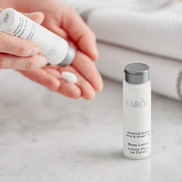 A person holding a small white bottle of Babor Energizing Lime & Green Tea lotion.