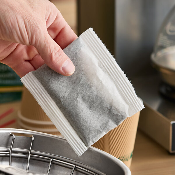 A hand holding a Folgers Classic Decaf 4-cup coffee filter pack above a coffee maker basket.