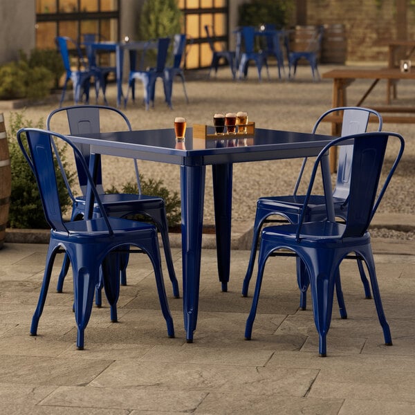 A blue metal Lancaster Table & Seating outdoor table with four chairs on a patio.