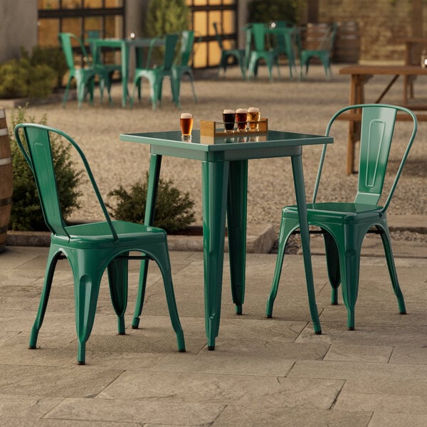 A Lancaster Table & Seating emerald green outdoor table with chairs on a stone patio.