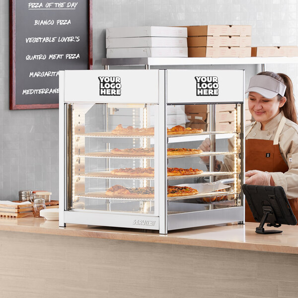 A woman standing behind a ServIt countertop display warmer with pizza inside.