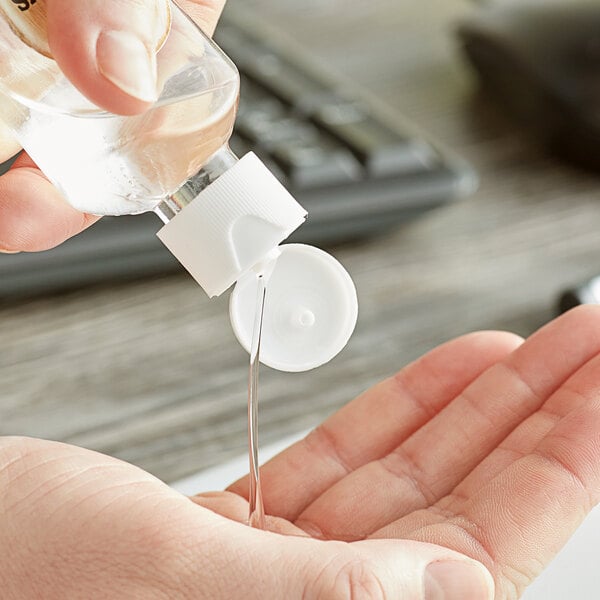 A hand pouring liquid from a small bottle into another white container using a 20/410 white unlined flip top lid.