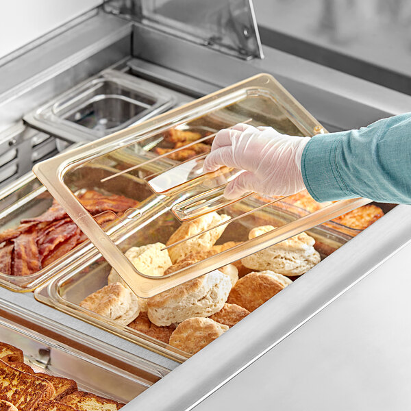 A person taking food out of a Cambro H-Pan with a handled flat lid.