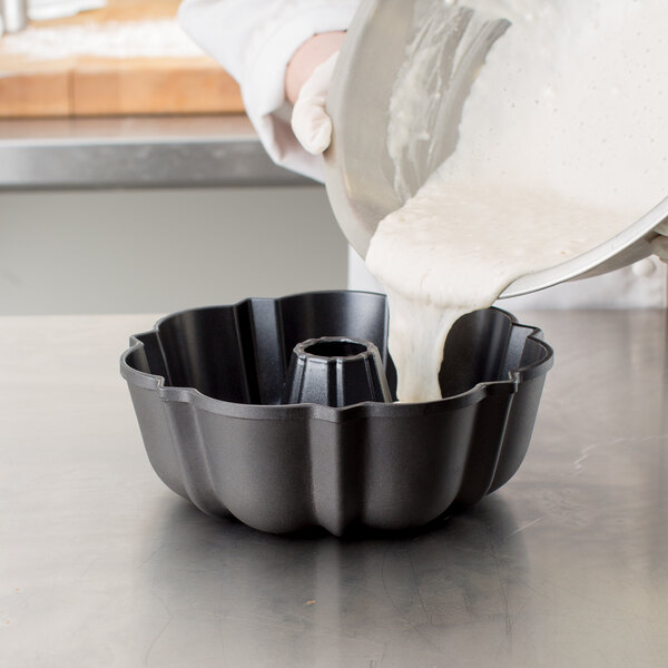 A person pouring white batter into a Chicago Metallic fluted bundt cake pan.