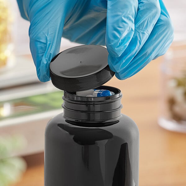 A gloved hand opens a black plastic bottle with a black ribbed cap.