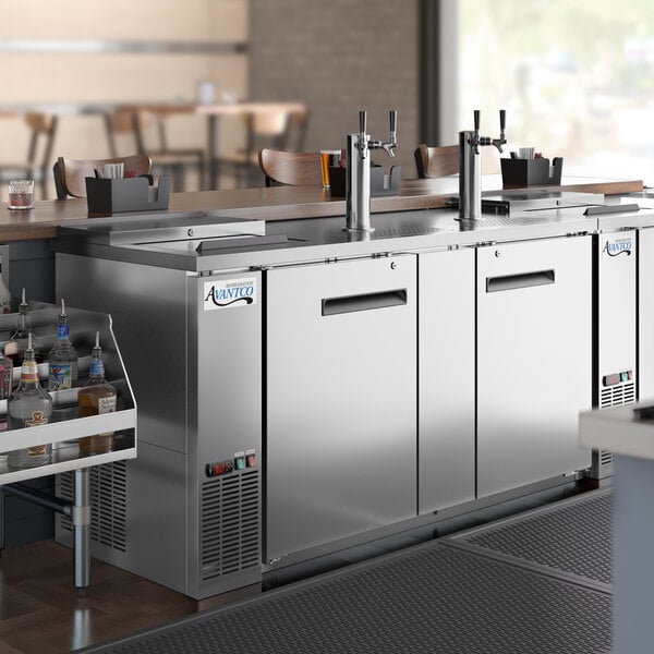An Avantco stainless steel kegerator with double taps on a large stainless steel counter.