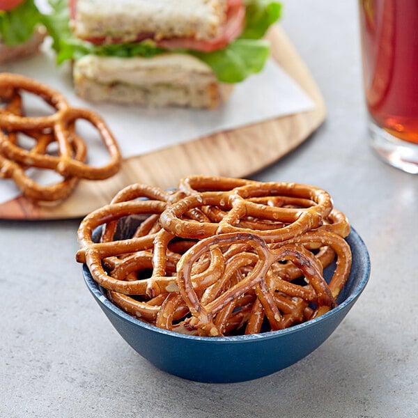 A bowl of Tom Sturgis thin pretzels next to a sandwich.