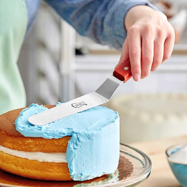 An offset spatula used to spread blue icing on a round cake