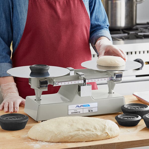 A mechanical baker's dough scale with two round weighing platforms and calibration weights, used for measuring dough portions.