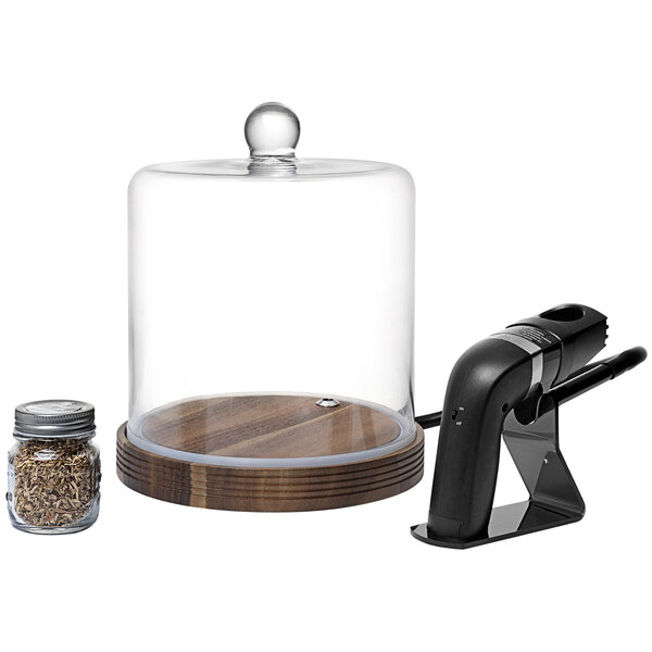 A Fortessa Crafthouse Classic Smoke Cloche with a glass bell jar on a wooden surface containing a jar of wood chips.