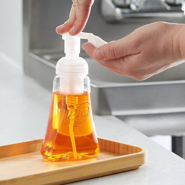 A person using Dial Citrus Sunburst foaming hand soap to fill a soap dispenser on a home kitchen counter.