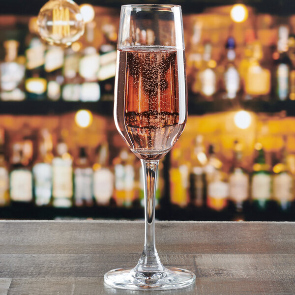 An Anchor Hocking Florentine II flute glass filled with pink champagne on a table in a bar.
