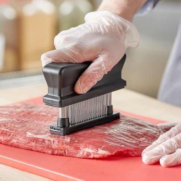 A hand in a plastic glove using a Choice 48-Blade Meat Tenderizer on meat.