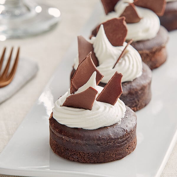 A row of chocolate cupcakes topped with Mona Lisa dark chocolate flakes on a white plate.