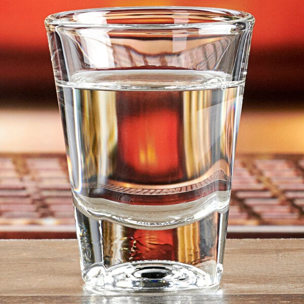 An Anchor Hocking double shot glass filled with water on a table.