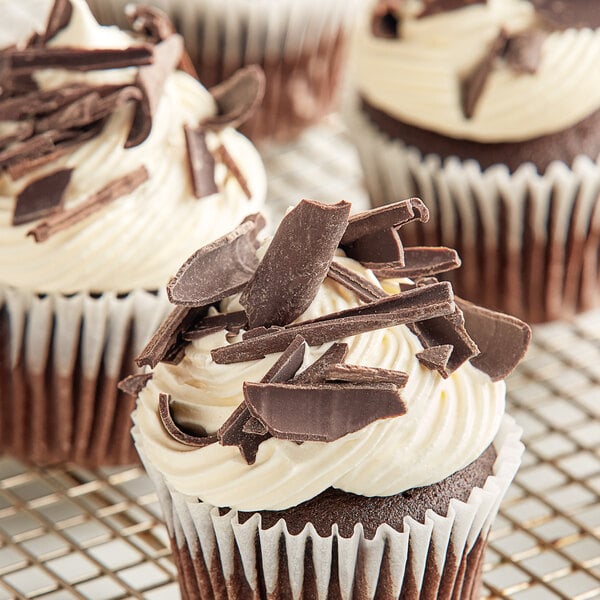 A chocolate cupcake with white frosting and Mona Lisa semi-sweet chocolate shavings.
