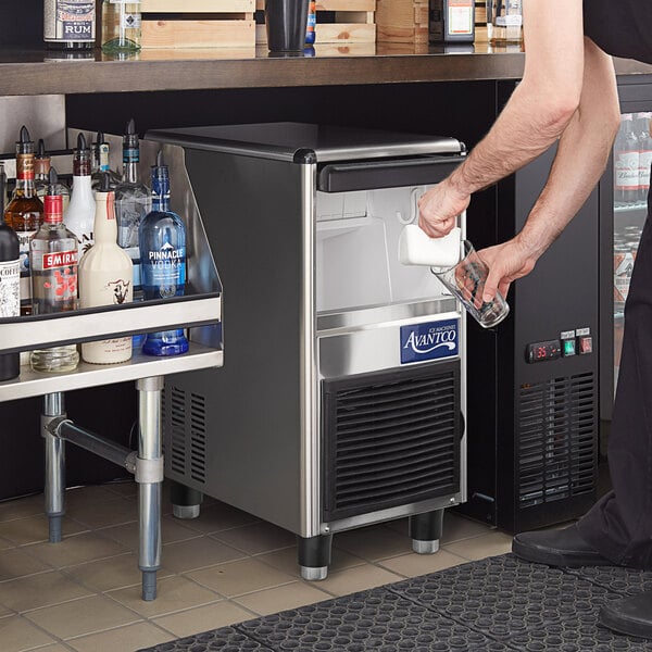 A man pouring a glass of ice from an Avantco undercounter ice machine.